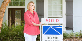 woman standing next to sold realty sign