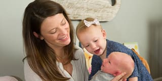 mother and toddler smiling at newborn
