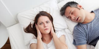 woman with hands over her ears with husband sleeping
