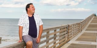 slightly smiling man leaning on a boardwalk at the beach