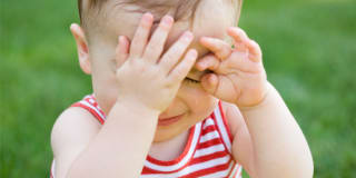 An crying baby sitting in the middle of the grass