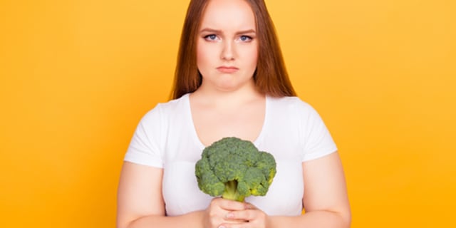 Girl looking sad holding a stalk of broccoli