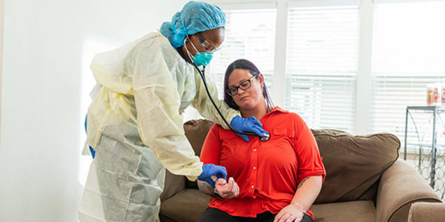 woman sitting on couch being examined by a gowned healthcare worker