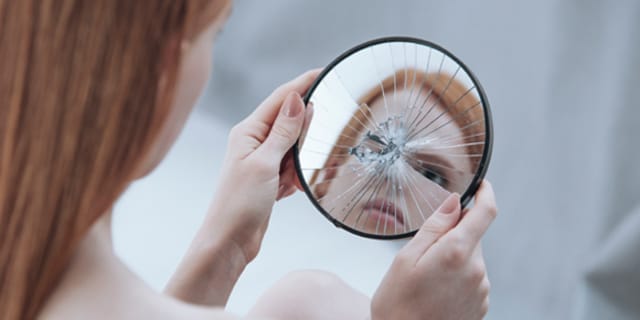 A woman looking at a broken mirror