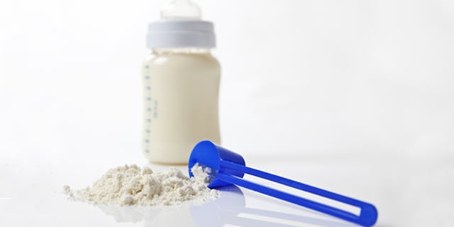 A close-up shot of baby milk formula with a plastic measuring spoon and bottle