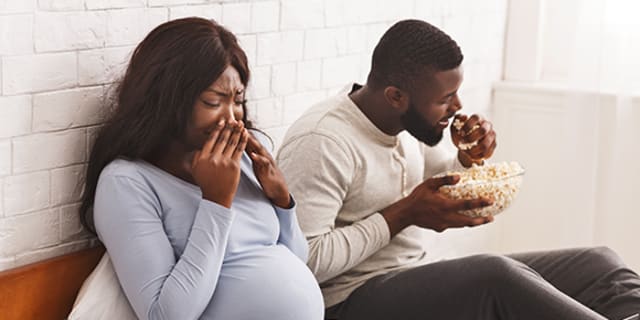 pregnant women with hands to her nose experiencing sensitivity of smell to man eating popcorn