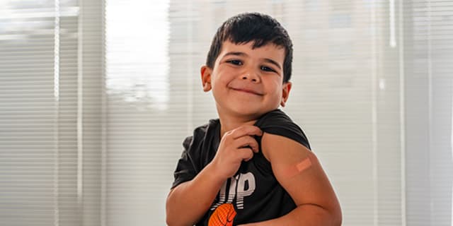 Little boy shows off bandage on upper arm regarding a shot