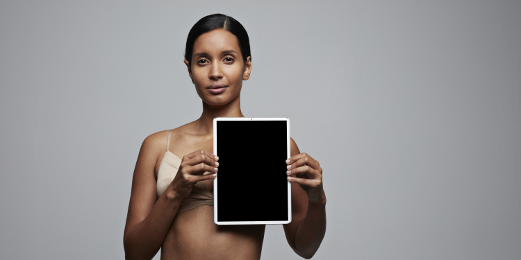 woman in underwear standing against a neutral background and holding a screen over her left breast