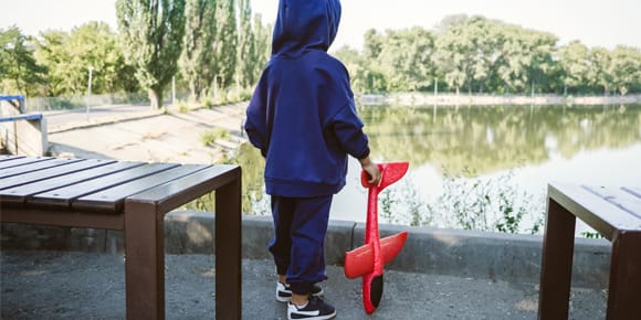 photo of the back of a child wearing a blue hoodie and holding a red toy airplane looking out over a pond
