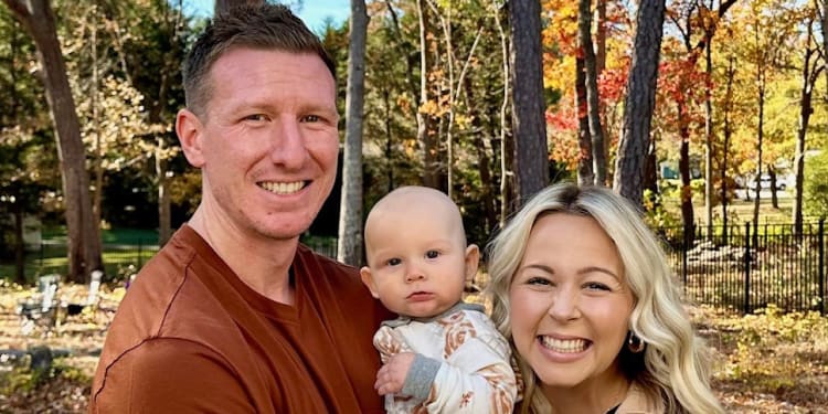 smiling couple holding a baby outside during fall