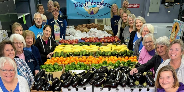a large group of volunteers at pie in the sky surrounded by boxes and crates of fresh fruits and vegetables.