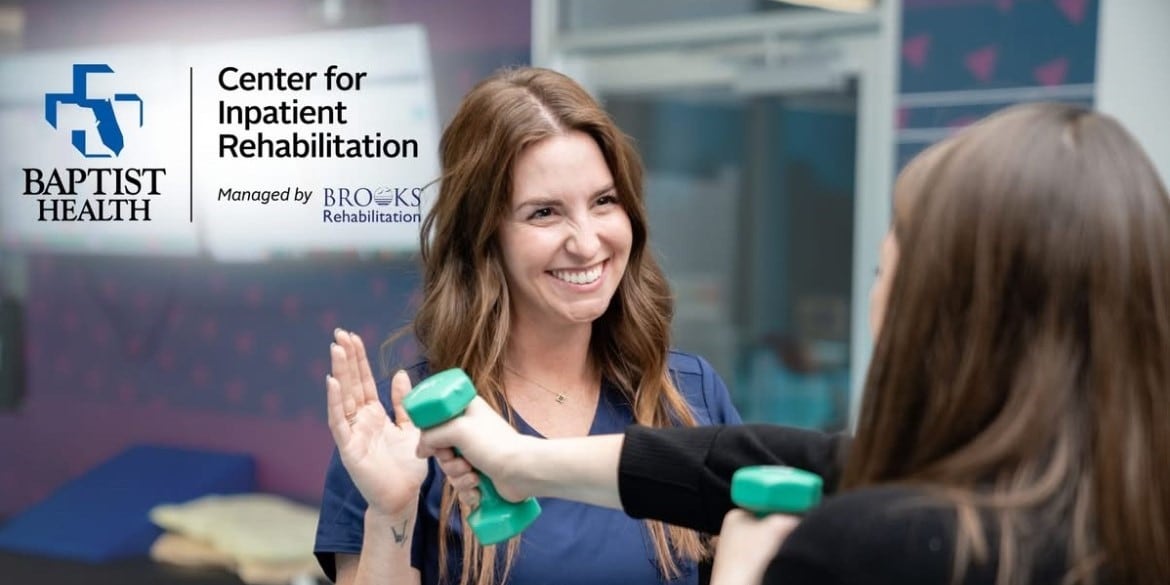 woman uses dumbbells while a therapist looks on