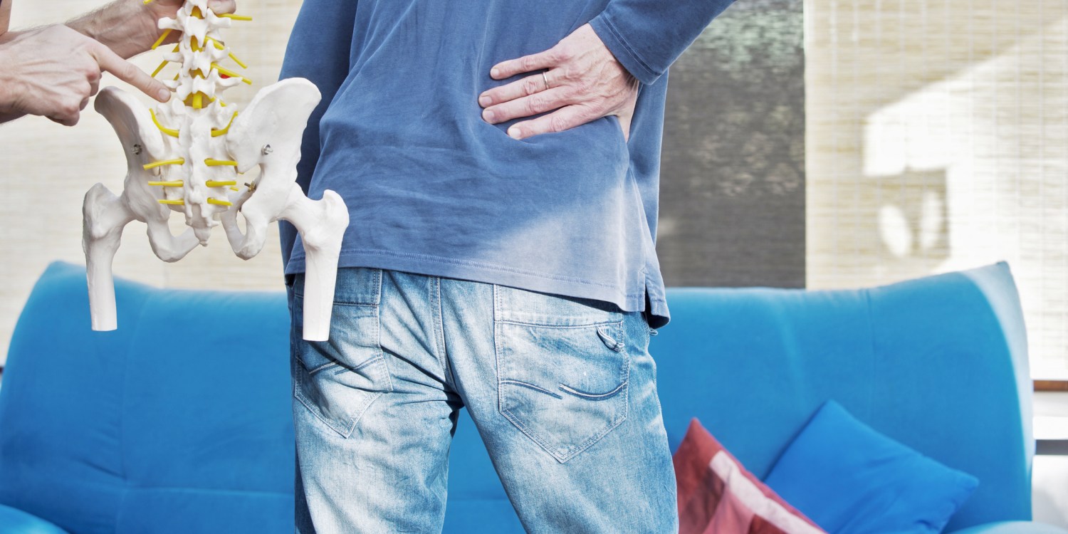 Doctor holding model of lumbar spine and nerves while man holds back in pain