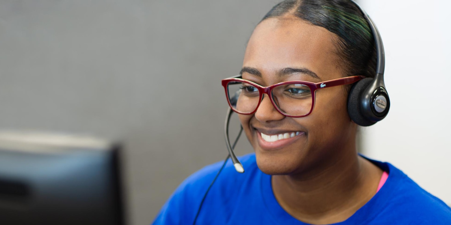 smiling woman sitting at a computer wearing a headset