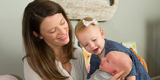 mother and toddler smiling at newborn