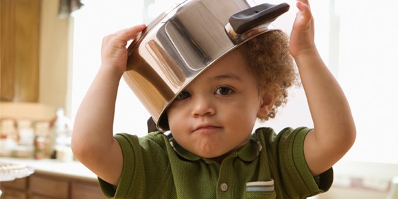 small boy in a green shirt with a large pot on his head