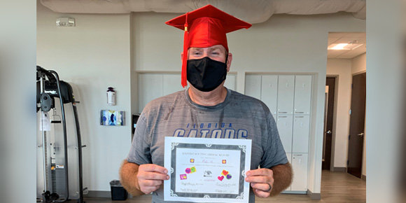 man wearing a graduation cap and mask while holding a diploma