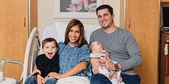 happy family sits in hospital bed with new baby