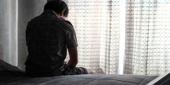 the view from behind a man sitting on the edge of a bed looking out the window