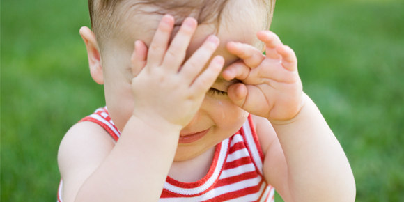 An crying baby sitting in the middle of the grass
