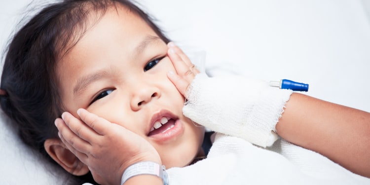 A sick asian child girl is lying on the bed and touching her face in the hospital