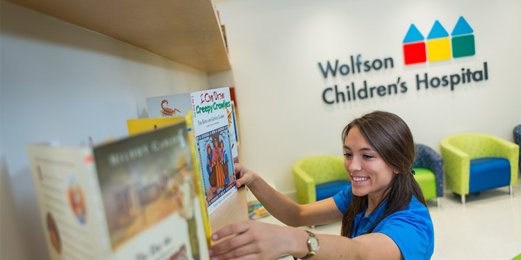 smiling young woman putting books on a bookshelf at Wolfson Children's Hospital