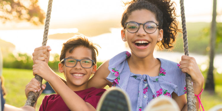 sister and brother outside on a swing smiling during a sunny day