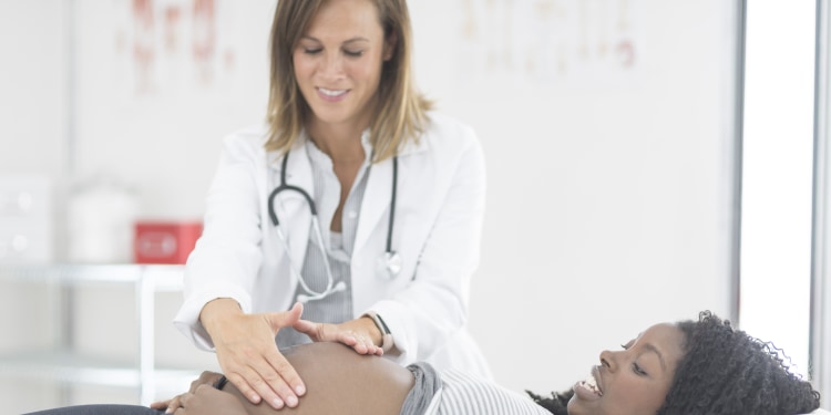 A pregnant woman is laying on an examination table at the doctor's office while a female physician exams her belly.