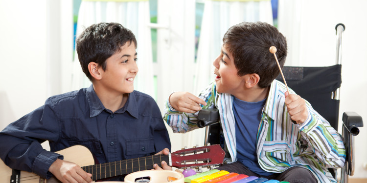 A young boy in a wheelchair plays the xylophone and another young boy plays the guitar