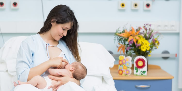 nursing mom with newborn baby and fresh bouquet of flowers by her bed in hospital birthing center