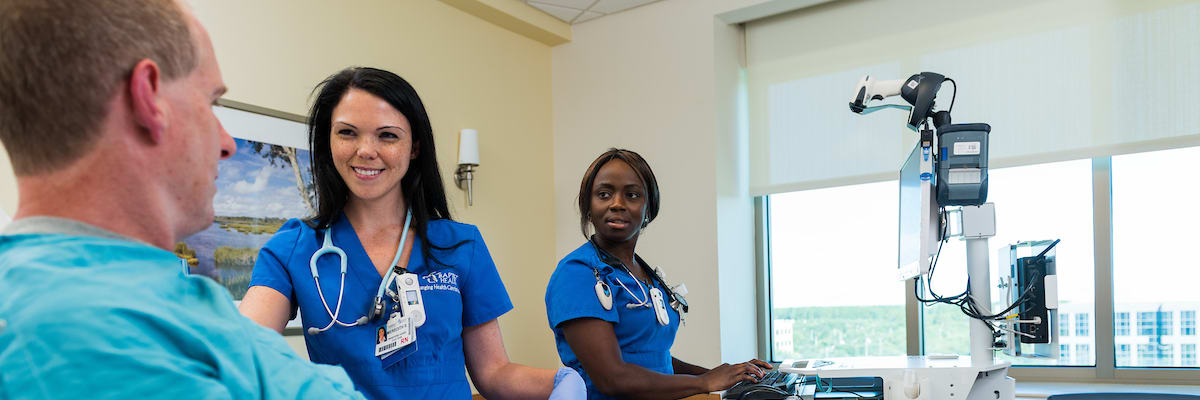 two female nurses caring for a male patient with smiles on their faces.