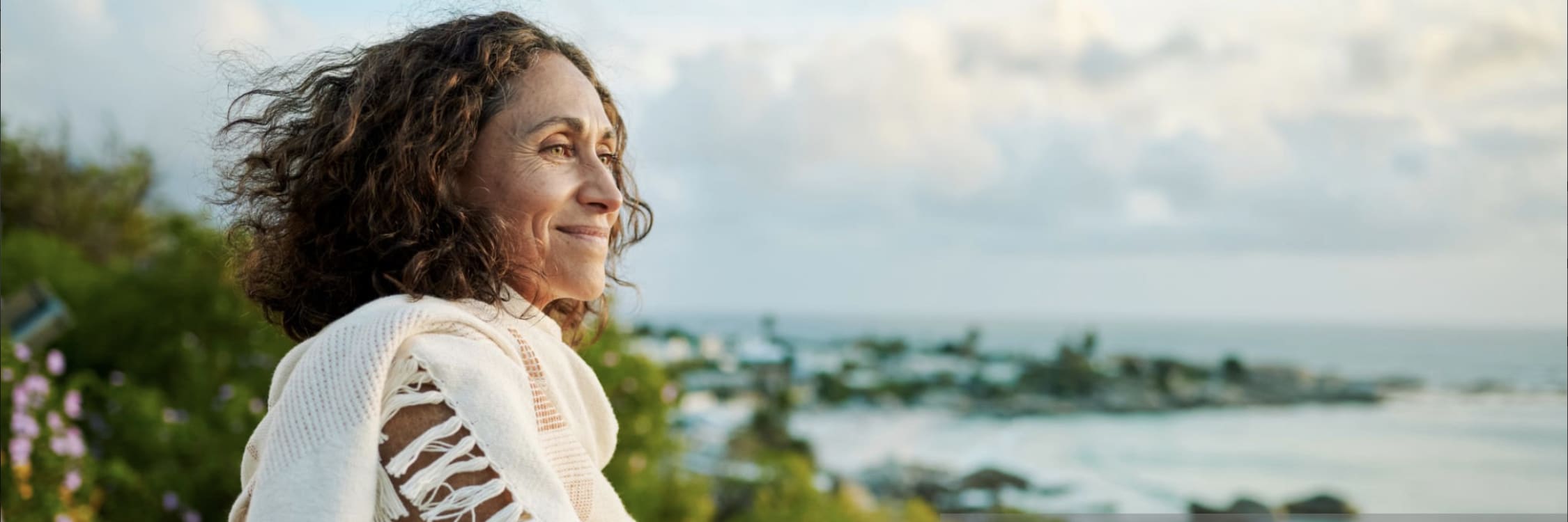 photo of a middle aged woman in a tropical setting looking out over the water and smiling