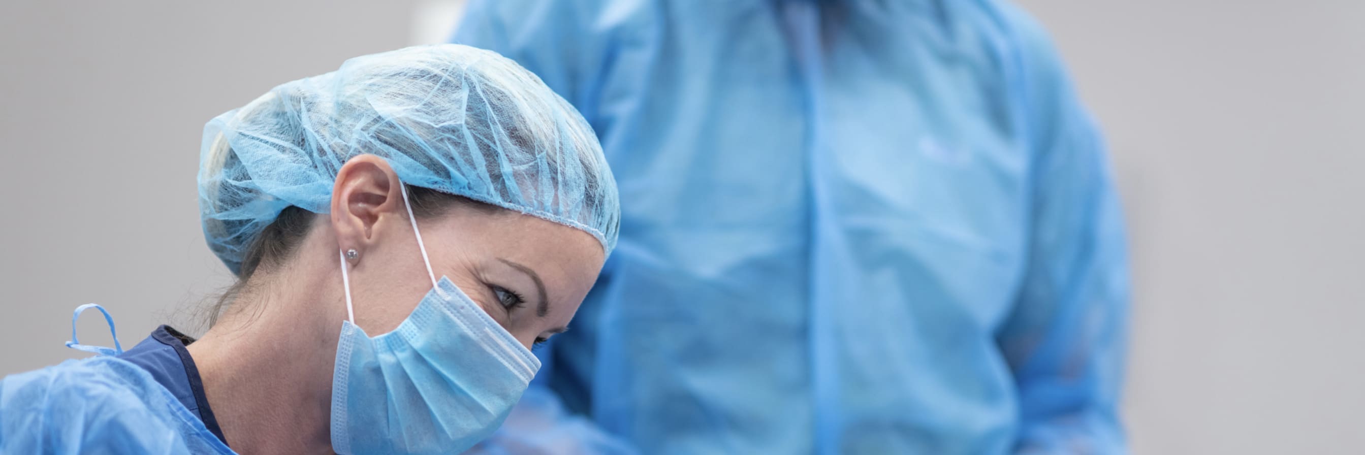 woman in surgical mask, gown and gloves holds patient's hand