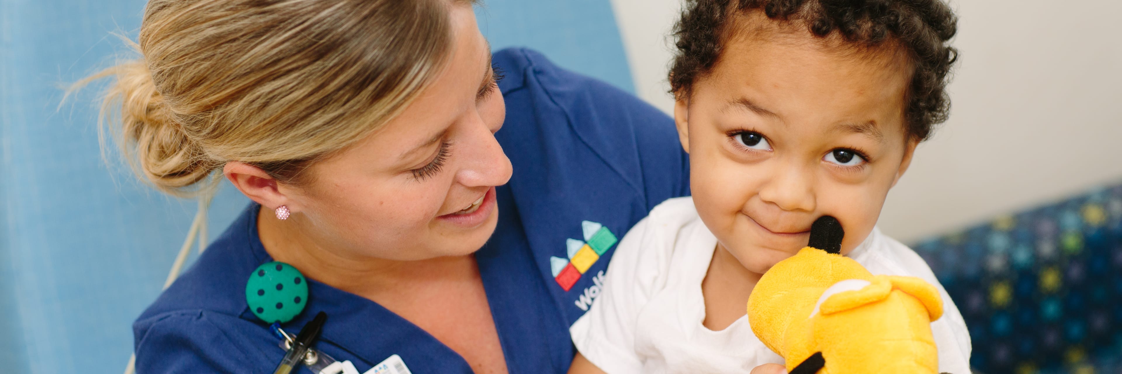 female Wolfson nurse holding a toddler smiling patient on her lap