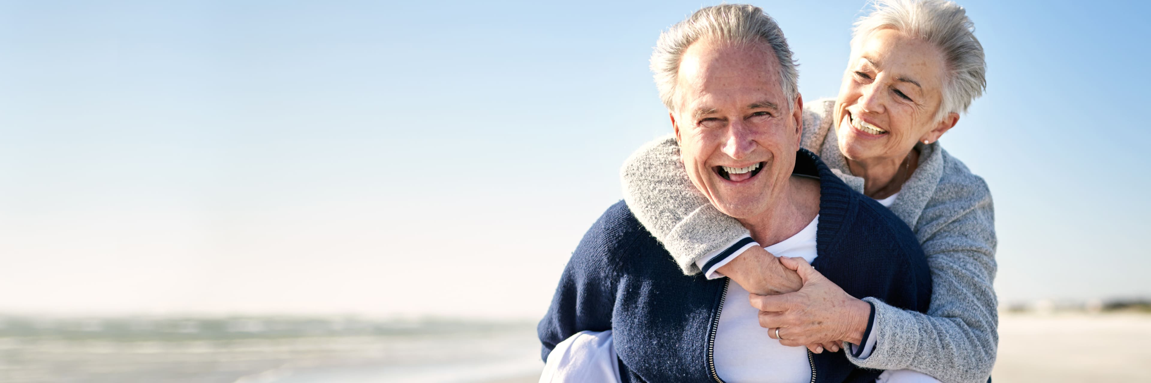 smiling man giving a smiling woman a piggyback ride on the beach