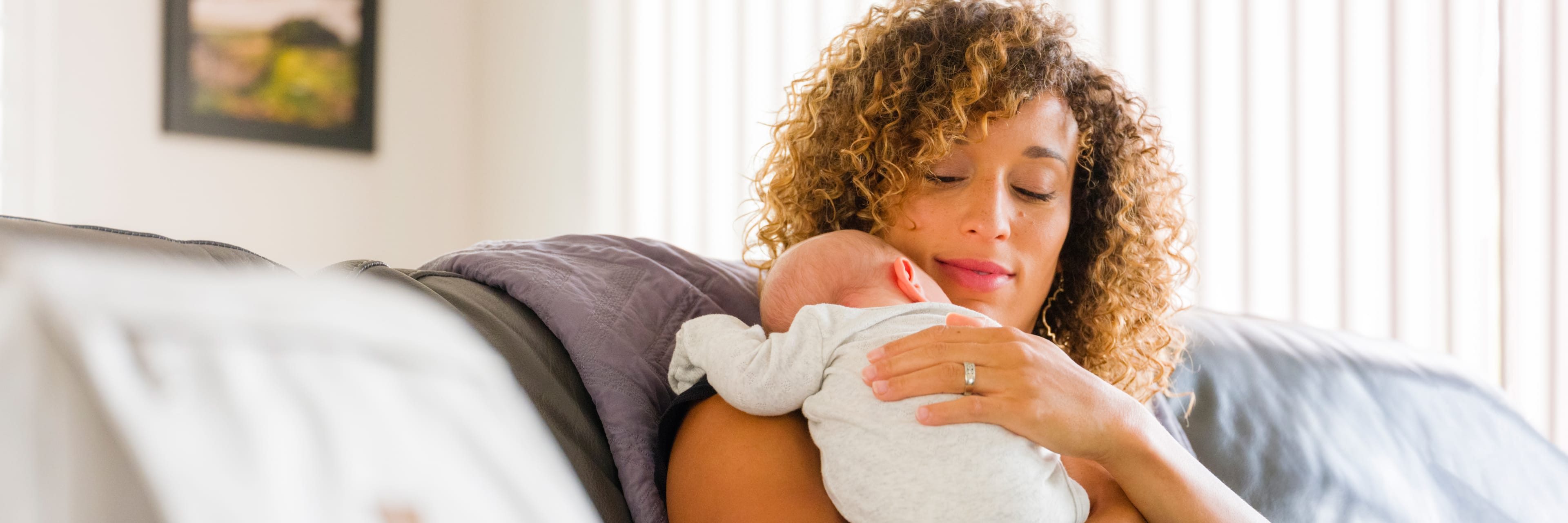 woman holds her new baby sitting on a couch