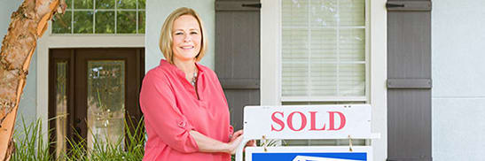 woman standing next to sold realty sign