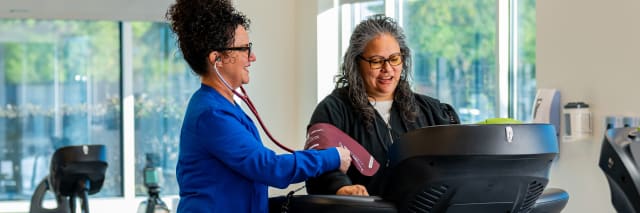 woman walks on a treadmill while a nurse looks on
