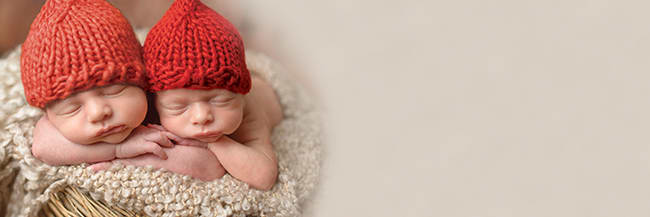 two newborns wearing red beanie hats