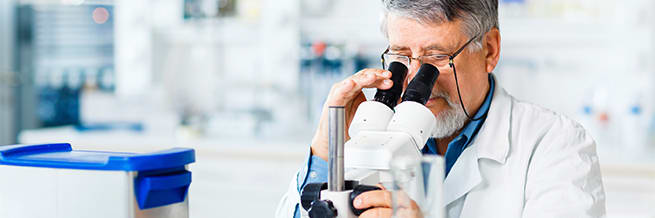 A doctor in a lab setting looks at a specimen through a microscope