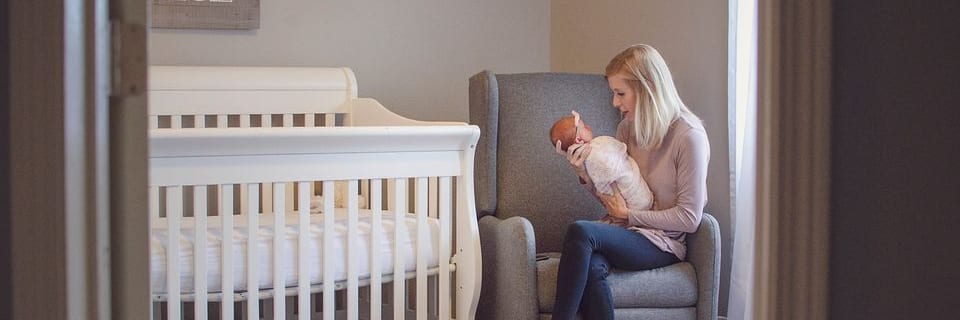 a new mom holding her baby while sitting in a chair in her baby's nursery.