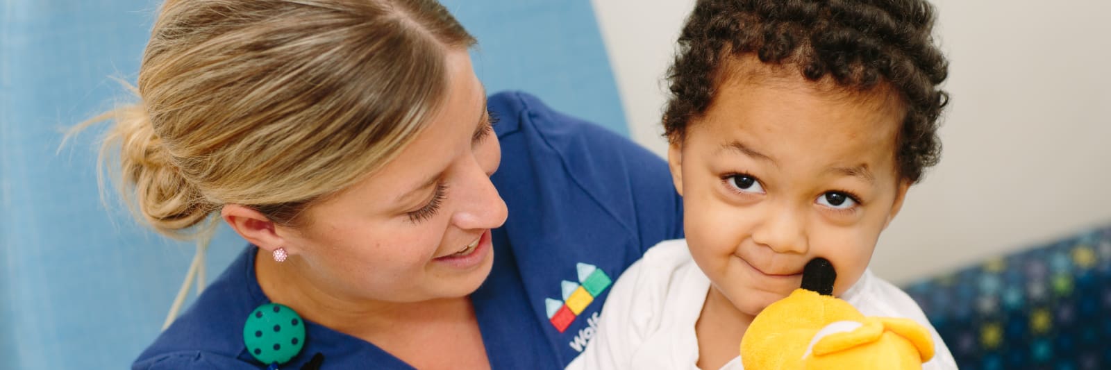 female Wolfson nurse holding a toddler smiling patient on her lap