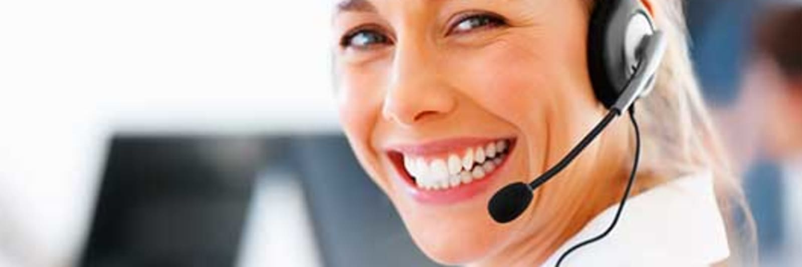 smiling blonde woman wearing a headset with computers in the background