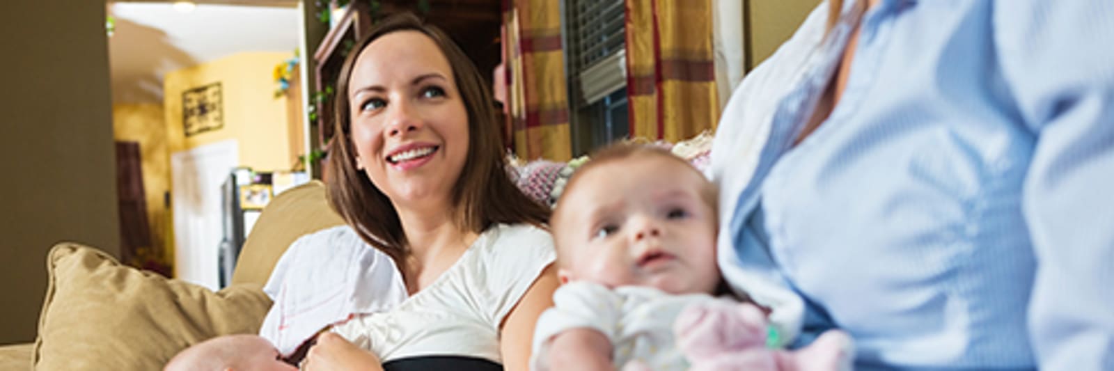 A mother is breastfeeding her baby and sitting next to another woman holding a baby
