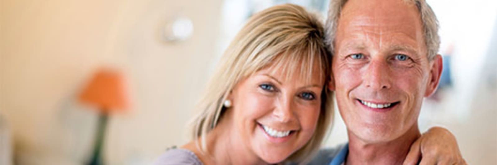 A smiling woman has her arms around a smiling man in a home setting