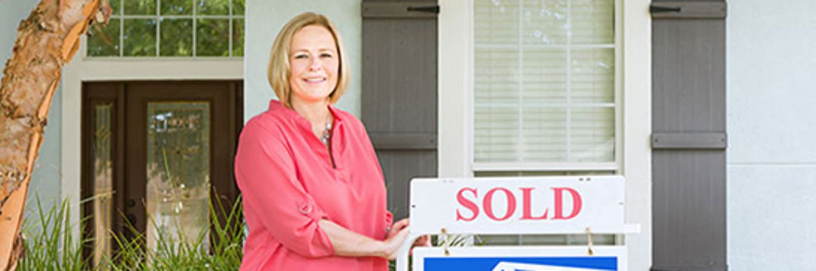 woman standing next to sold realty sign