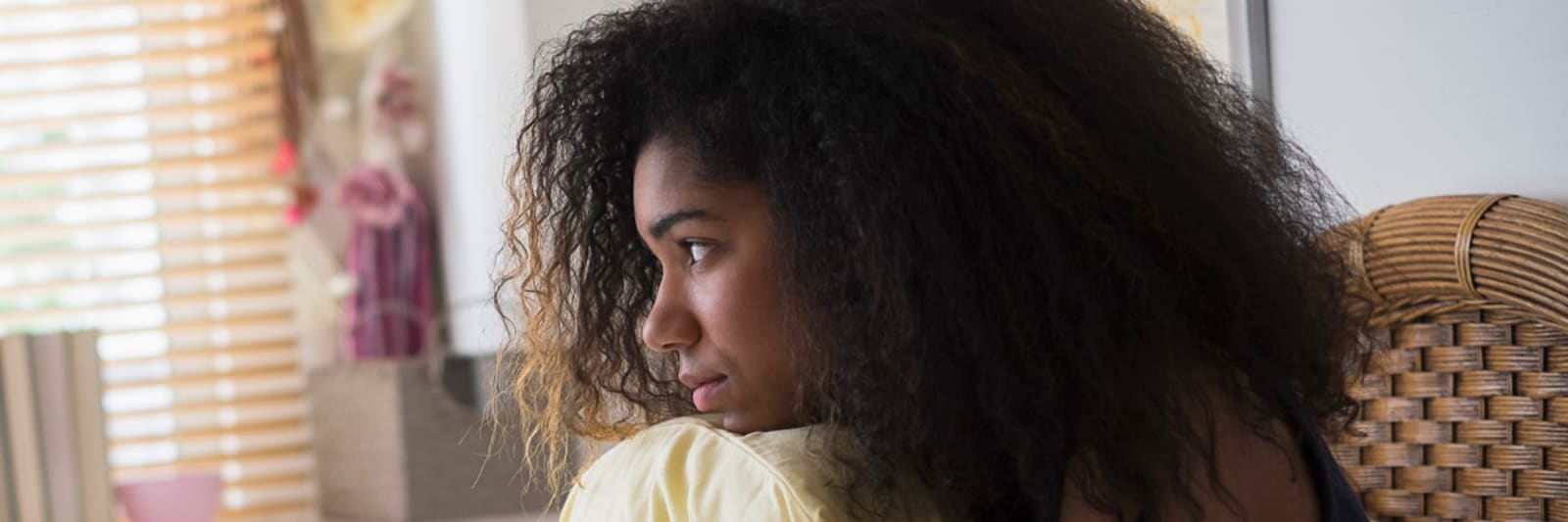 a teenage girl staring out the window of her bedroom hugging her pillow