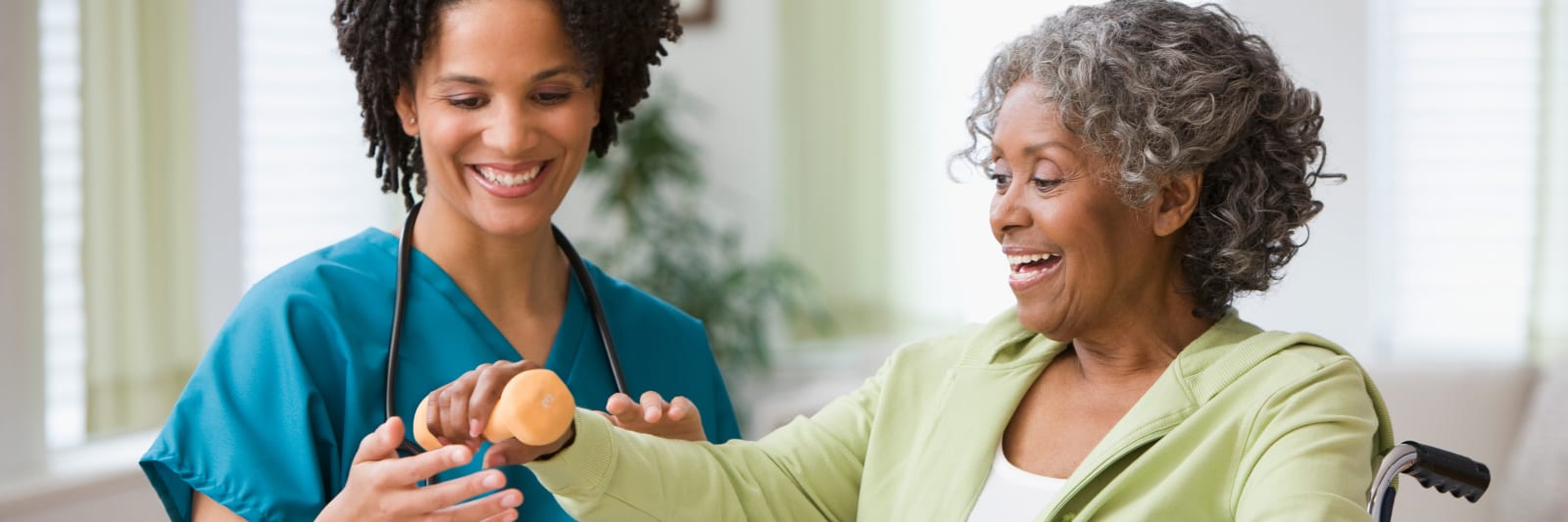 Smiling female nurse helping an elderly woman in a wheelchair lift a dumbbell