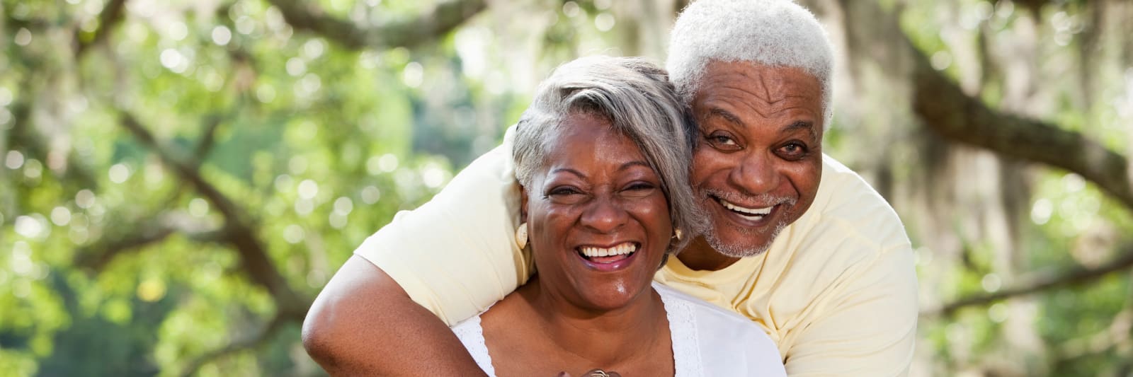 smiling husband and wife outside in front of trees