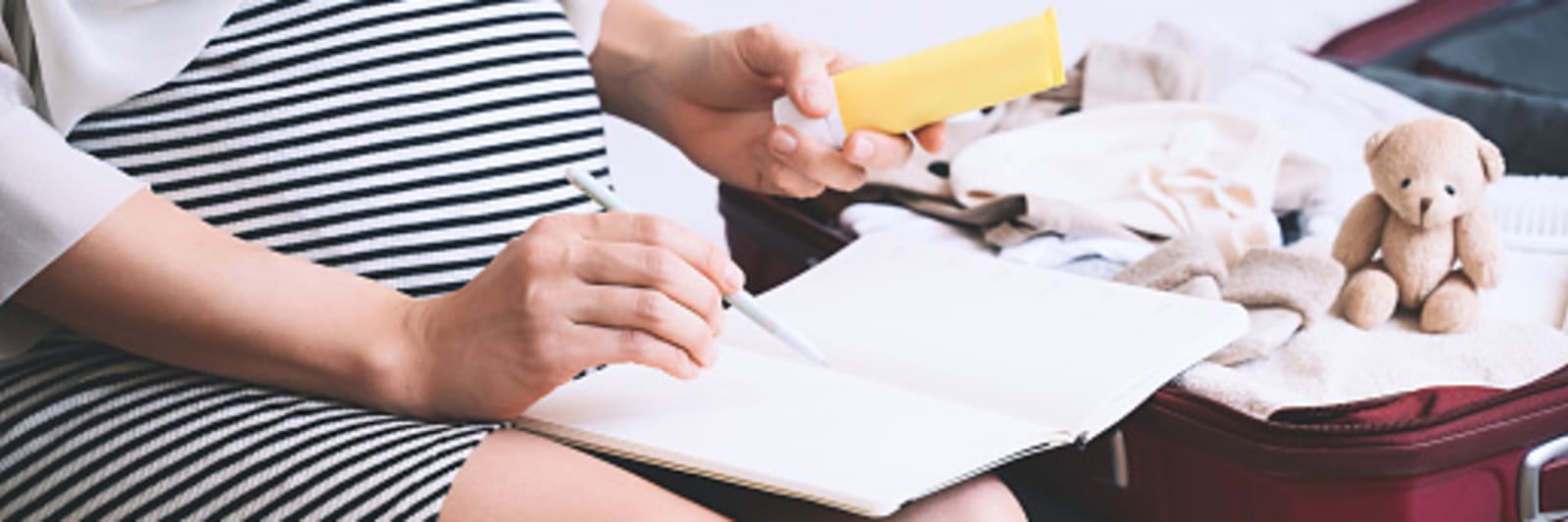 Pregnant woman packing hospital bag with checklist.